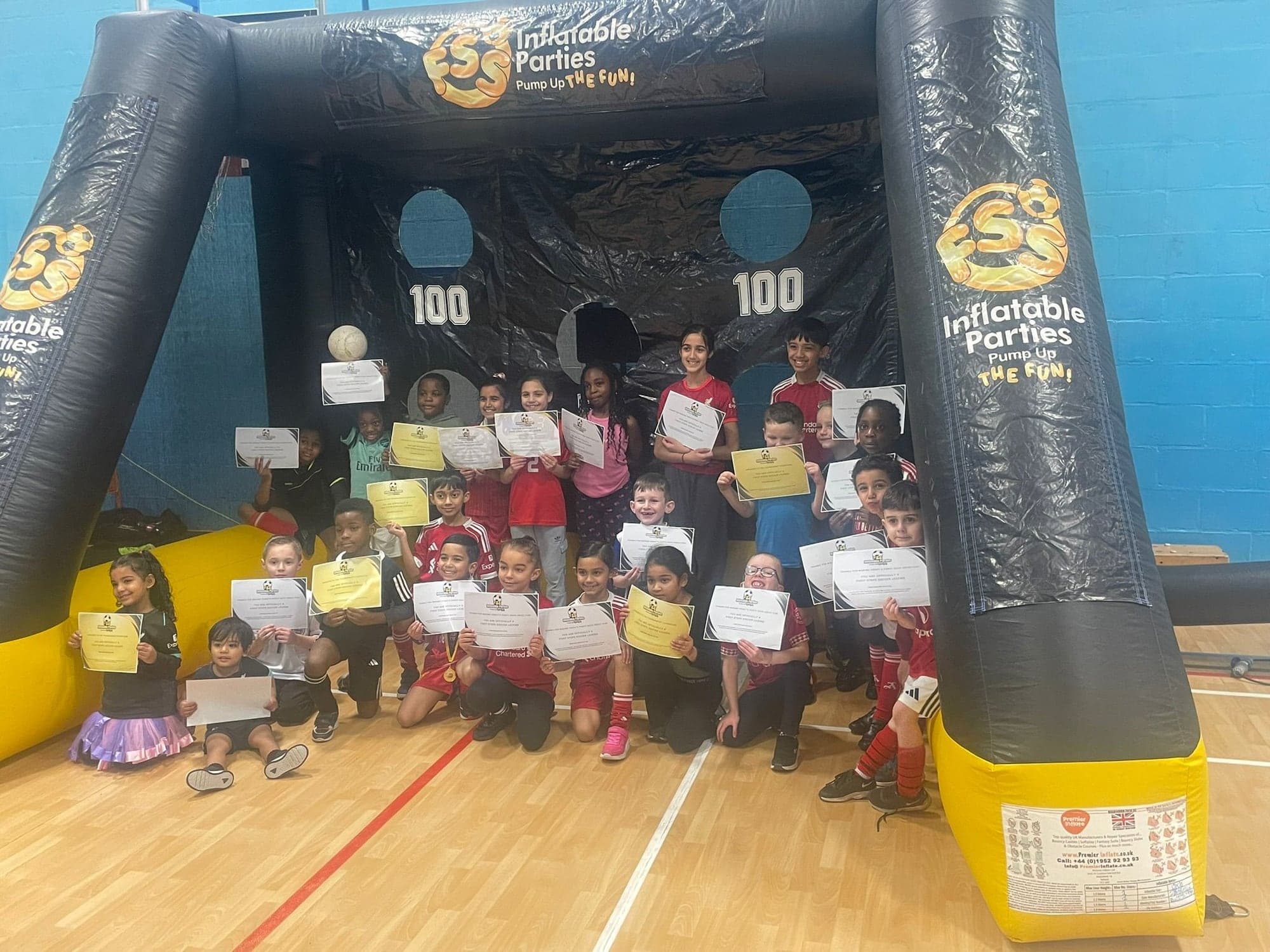 A big group of children holding their certificates in front of the FSS inflatable target goal